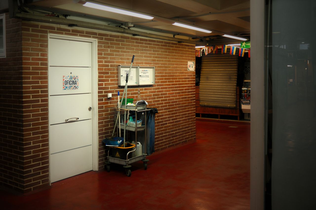 hero-img-01 A brightly lit industrial hallway with a cleaning cart and supplies near an office door.